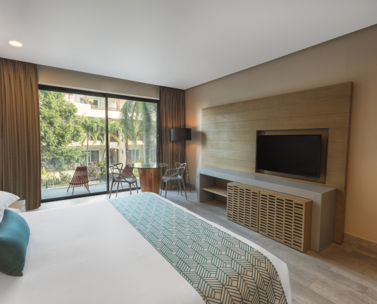 Dormitorio con cama King en esquina, televisor montado en la pared y mesa en la esquina de la habitación